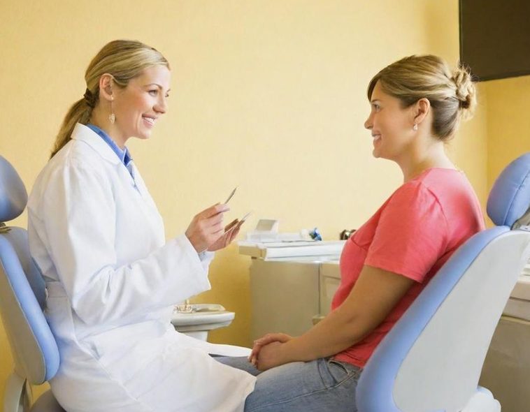 Zahnärztin spricht mit Patientin in einer Praxis, beide lächeln.