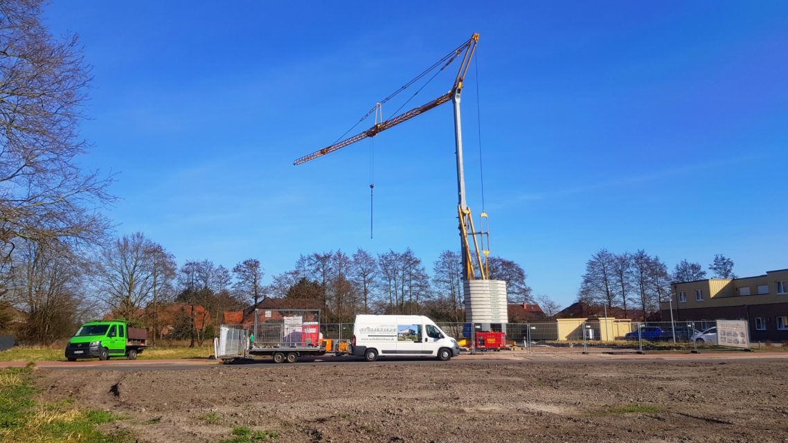 Kran wird benötigt Kran auf einer Baustelle mit Fahrzeugen und klar blauem Himmel im Hintergrund.