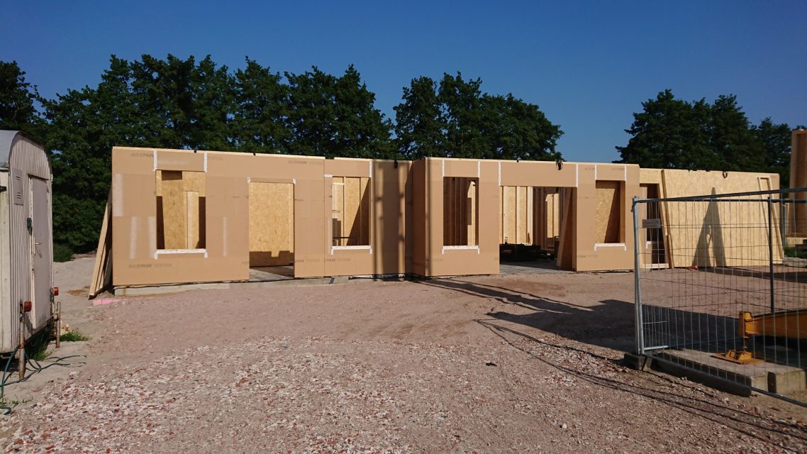 Wände & Fenster in Blockbauweise Rohbau eines Holzhauses mit offenen Fenstern und Türen unter klarem Himmel.