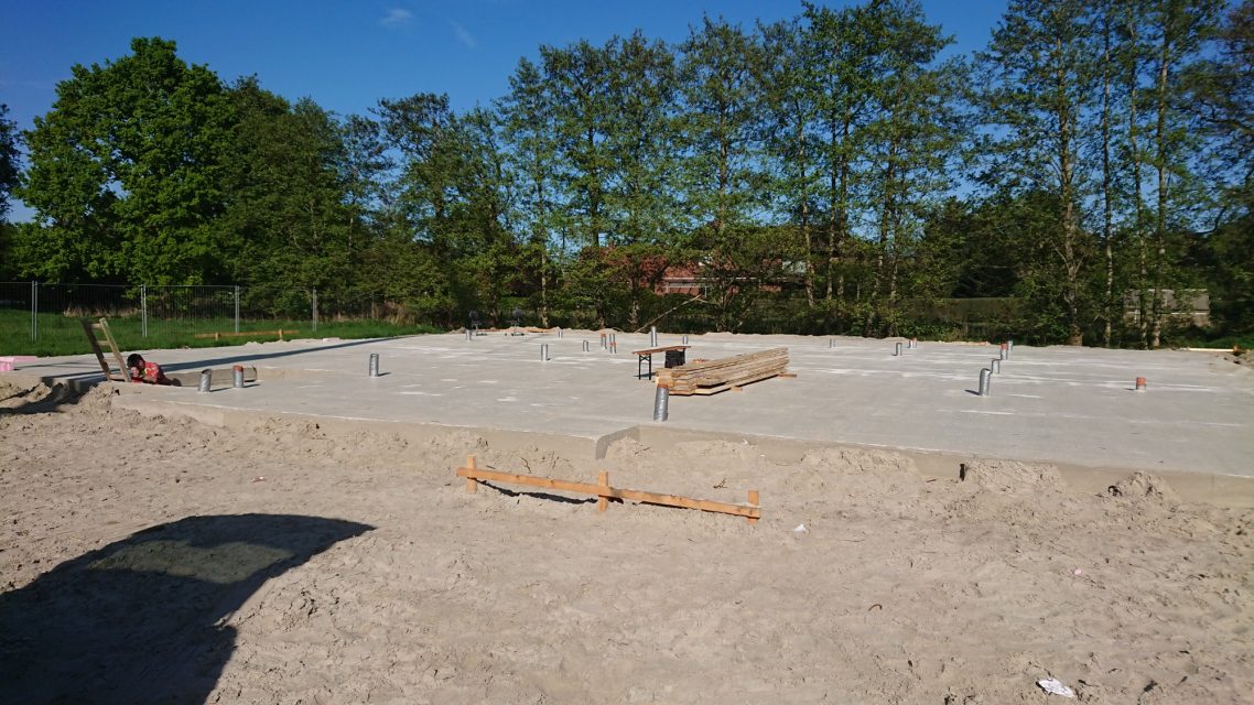 Frischer Beton Bauplatz mit frischem Beton, umgeben von Bäumen und einem klaren blauen Himmel.