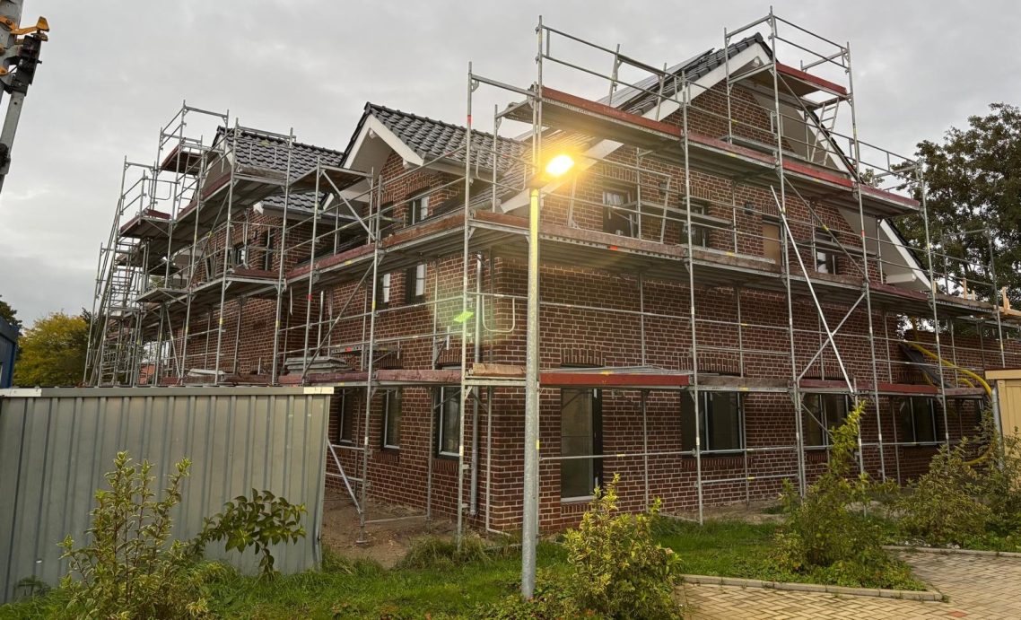 Außen ist bald alles fertig Neubaugebäude mit Gerüst und Außenarbeiten, umgeben von Bäumen und einem kleinen Lichtmast.