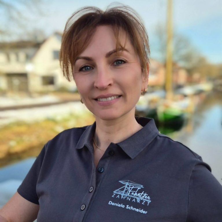 Lächelnder Mann in einem grauen Shirt vor einem Kanal und Wohngebäuden.