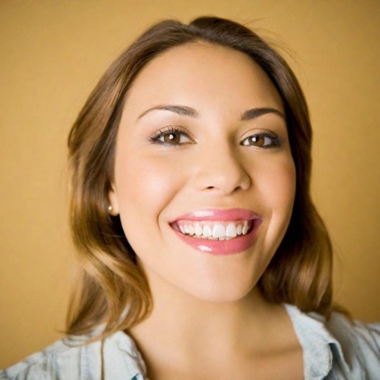 Lächelnde Frau mit langen, lockigen Haaren vor einem gelben Hintergrund.