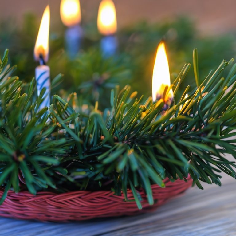 Weihnachtlicher Kranz mit brennenden Kerzen auf grünem Nadelholz.