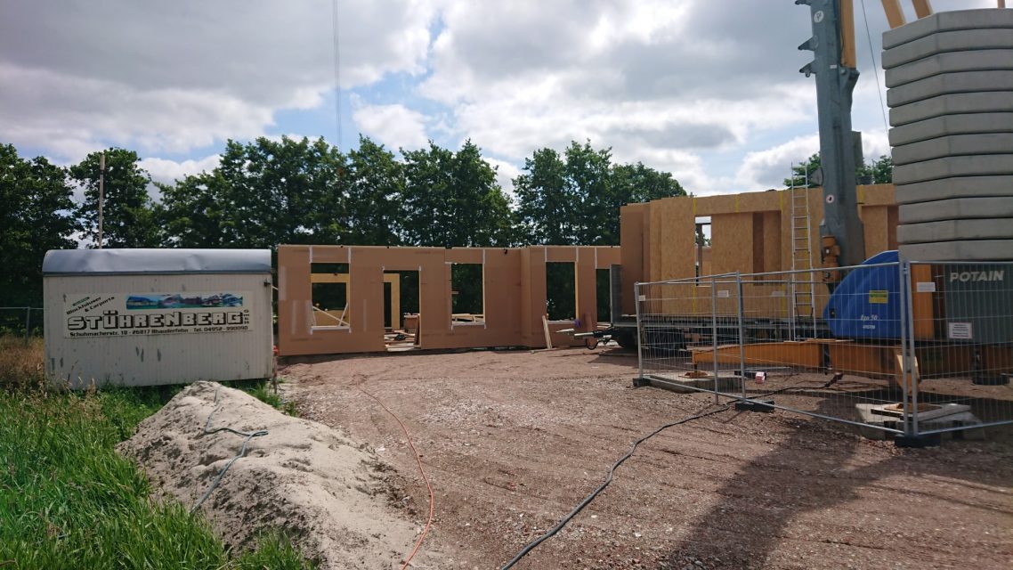 Die ersten Wände kommen Holzrahmenbau auf einer Baustelle mit Maschinen und Baustellencontainer.